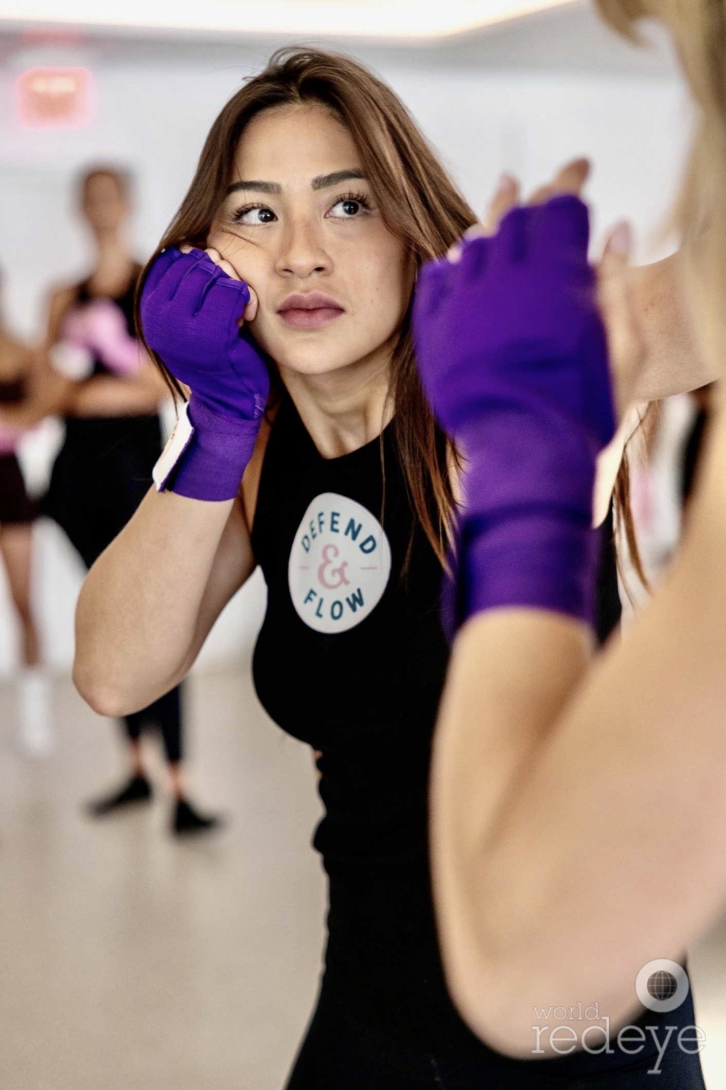 Close-up of a woman in a defensive boxing stance, purple hand wraps, focused expression.