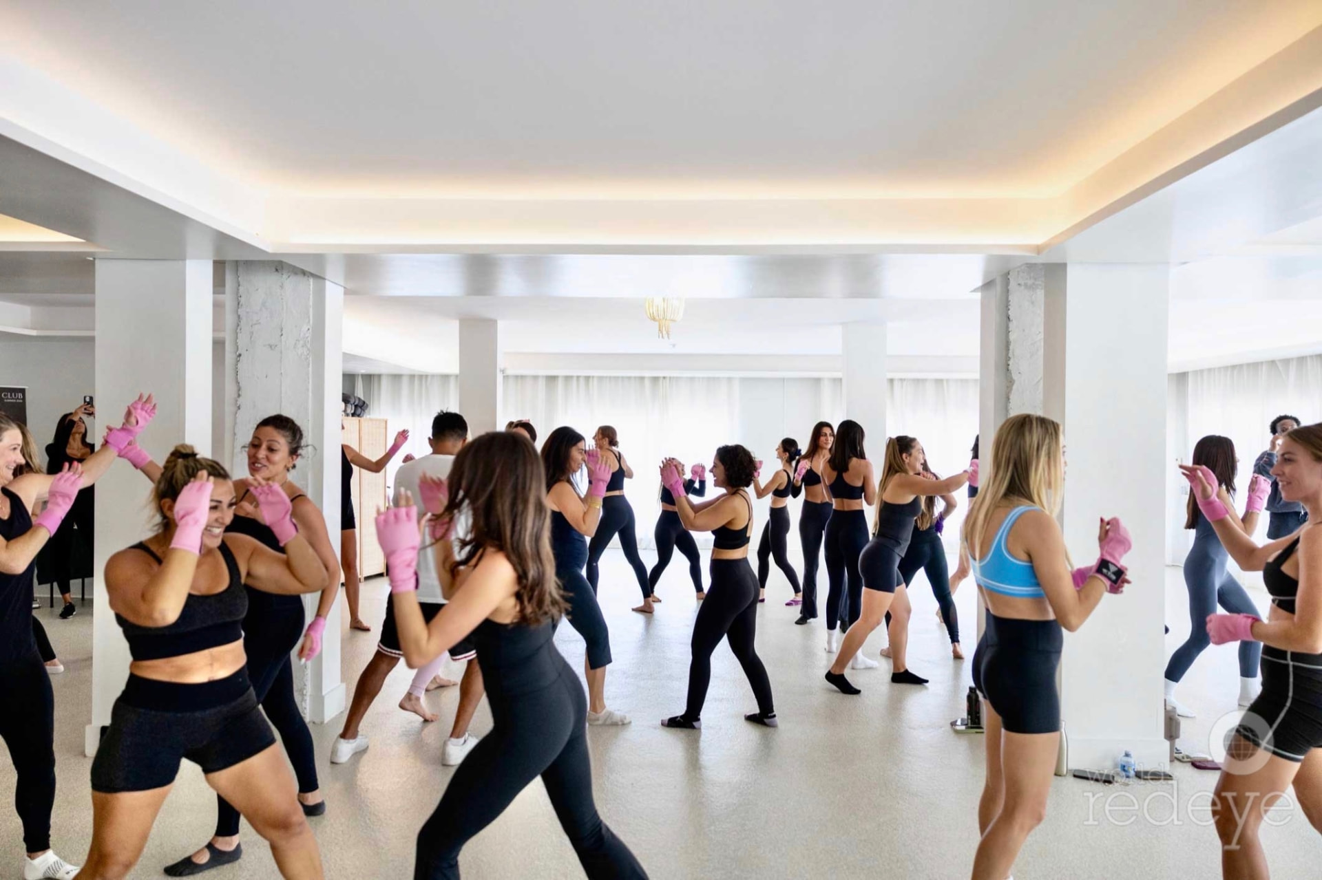 A large group of women in athletic wear practicing strikes together in the bright studio.