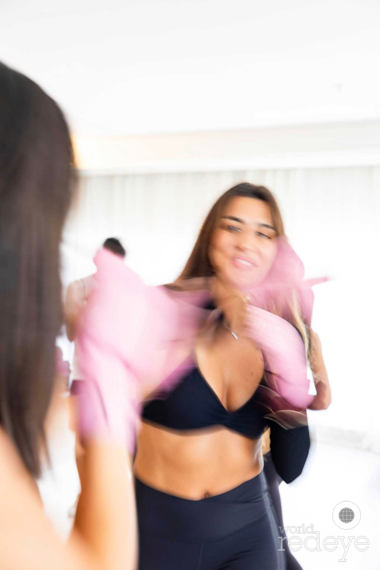 A woman in a black sports bra adjusts her pink hand wraps in motion across the bright studio.