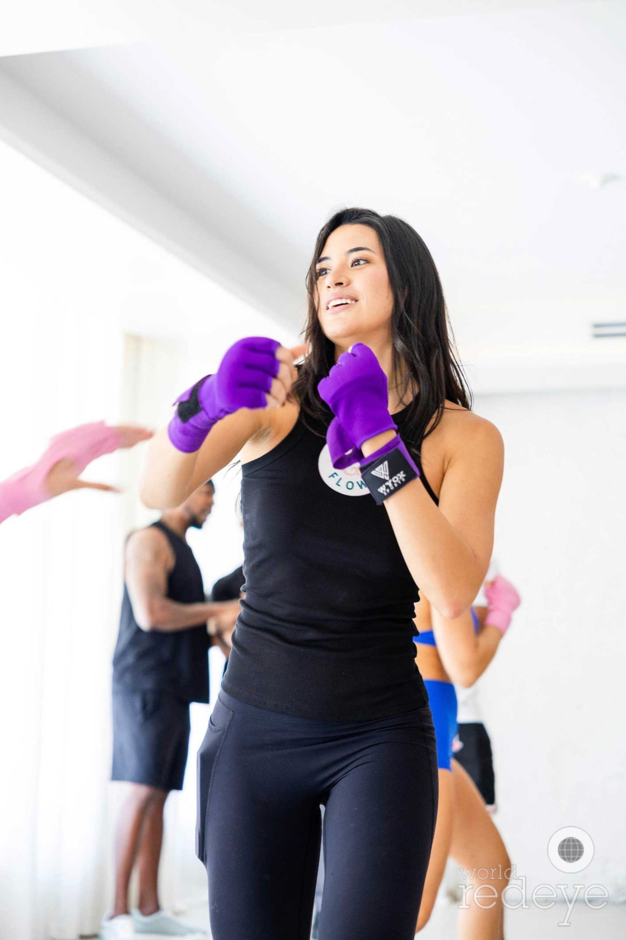 A woman in a Defend & Flow tank smiles mid-drill with purple hand wraps raised.