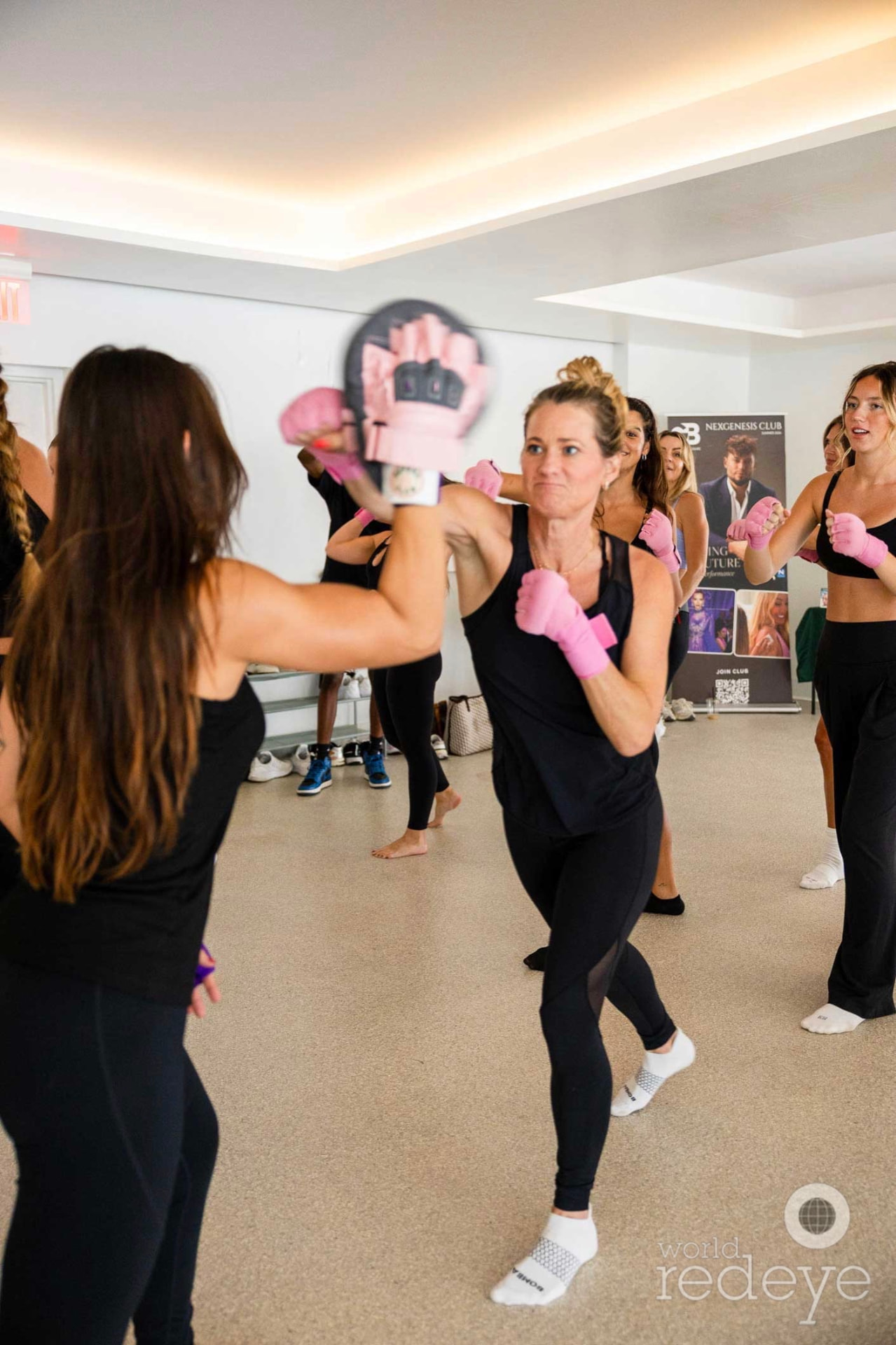 A woman in a black tank top strikes a pink focus mitt held by her partner.