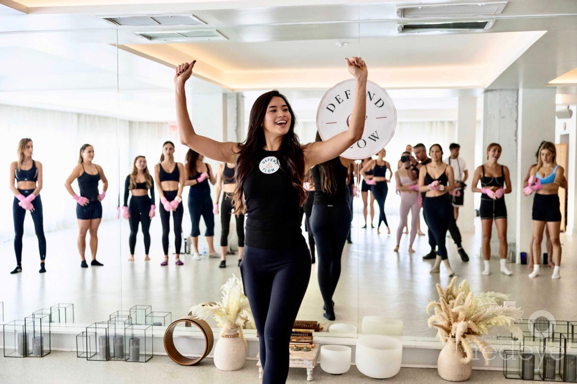 The instructor raises her arms in celebration in front of the mirrored Defend & Flow studio.