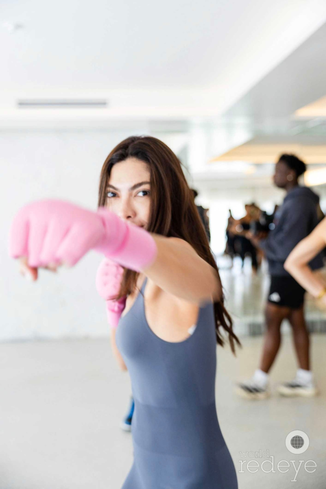 A woman in a grey bodysuit throws a focused punch toward the camera, pink wraps on.